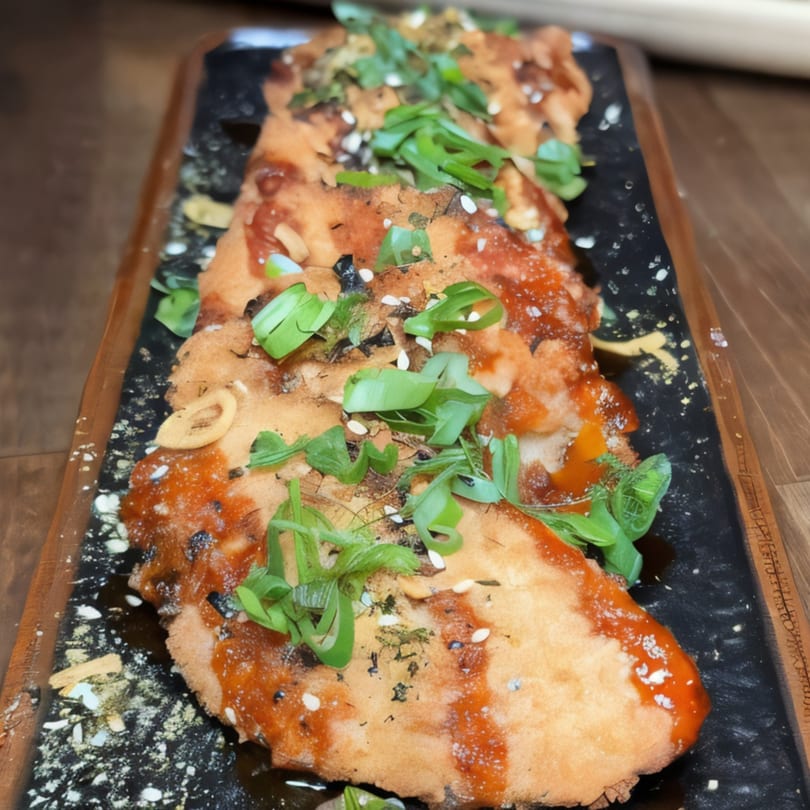 Crispy fried Asian-fusion dish with red sauce, green onions, and sesame seeds on a dark platter.