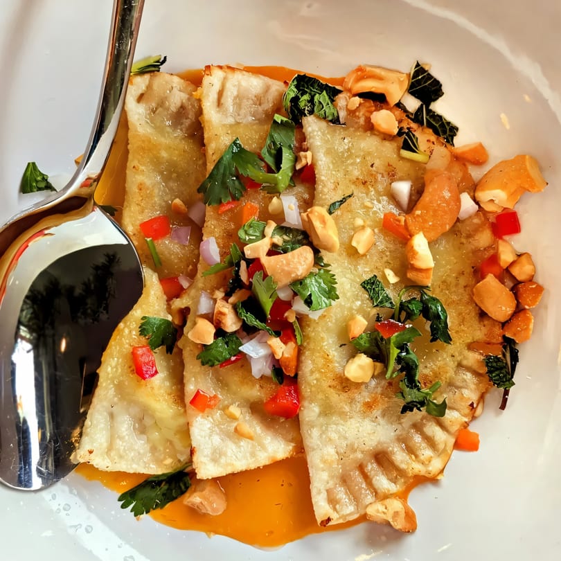 Crispy Kantina Kita dumplings with orange sauce, topped with peanuts, red peppers, and cilantro.